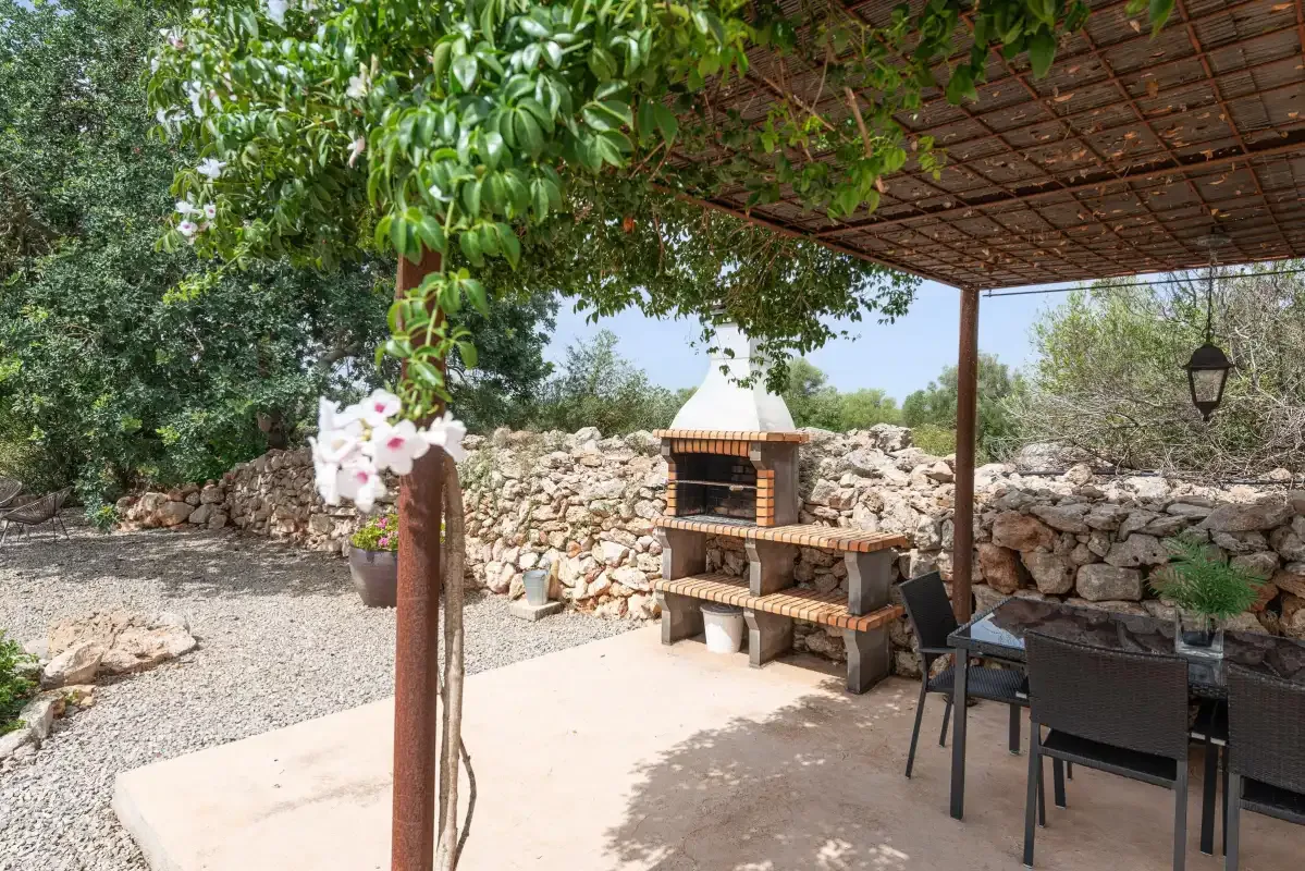A covered outdoor seating area with a built-in barbecue beside a stone wall.