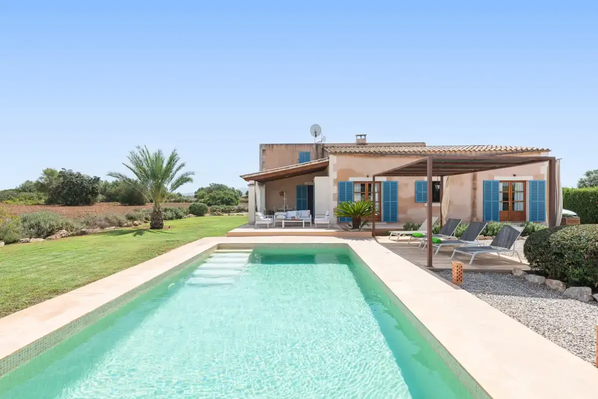 A swimming pool in front of a house, with lounge seating on the patio.