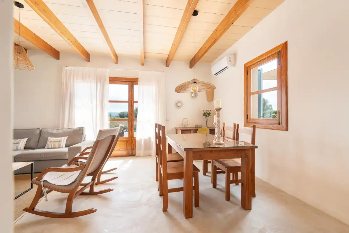 A bright dining and sitting area with wooden furniture and exposed ceiling beams.