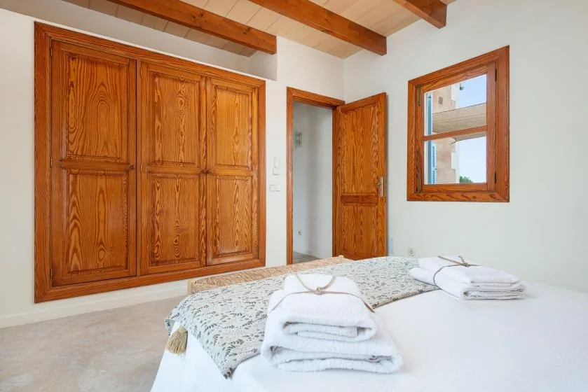 A bedroom with a bed, wooden built-in cupboards, and a window.