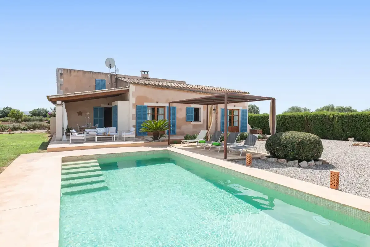 A house and swimming pool sit beside a patio with shaded seating.