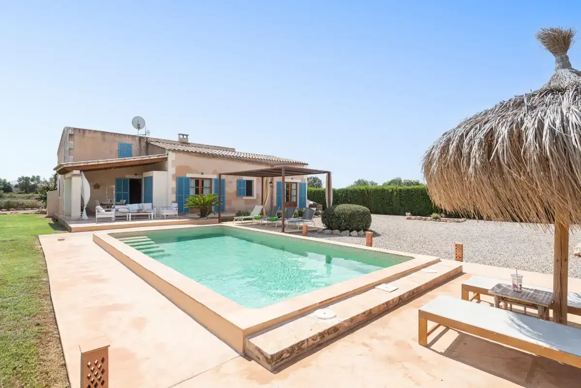 A swimming pool and sun loungers sit beside a house in a landscaped yard.