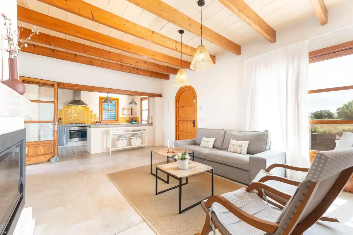 A bright living room with a gray sofa, armchairs, and an open kitchen.