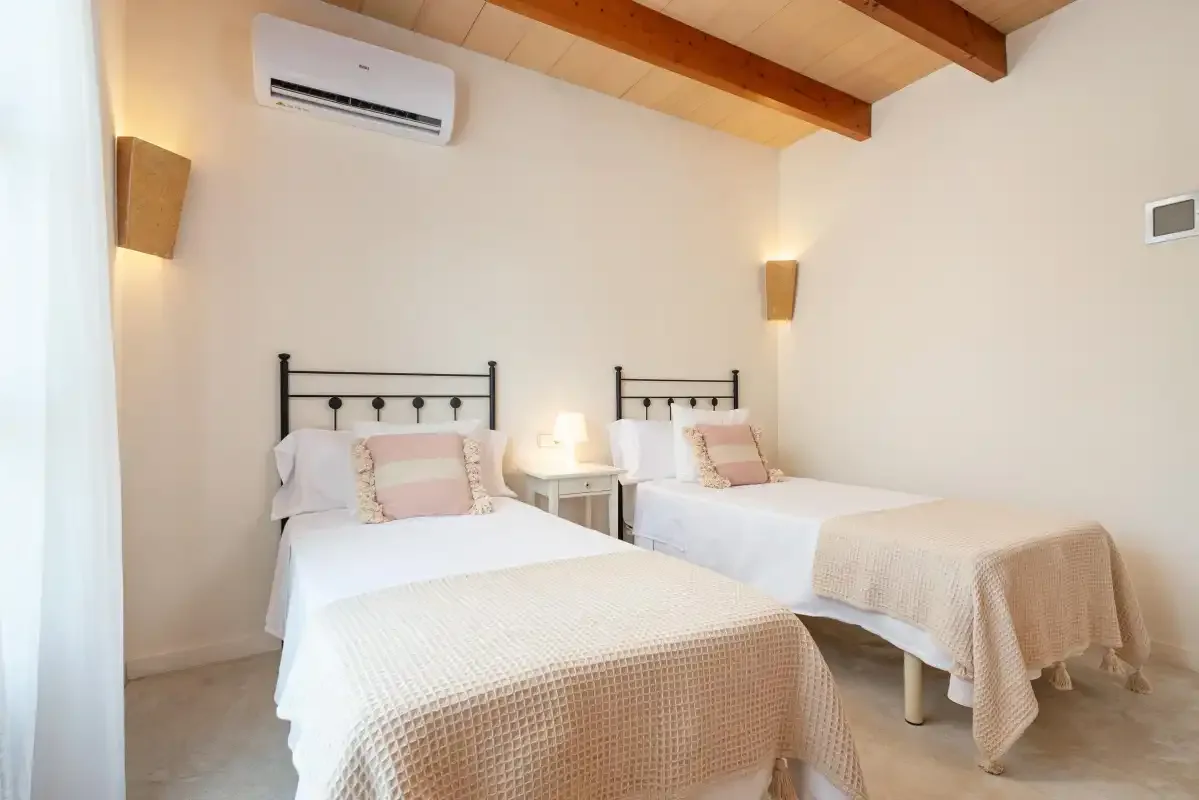 A bedroom with two beds and light-colored bedding beneath a wood-paneled ceiling.