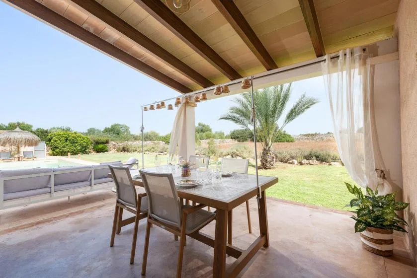 A covered outdoor dining area overlooks a lawn, palm tree, and swimming pool.