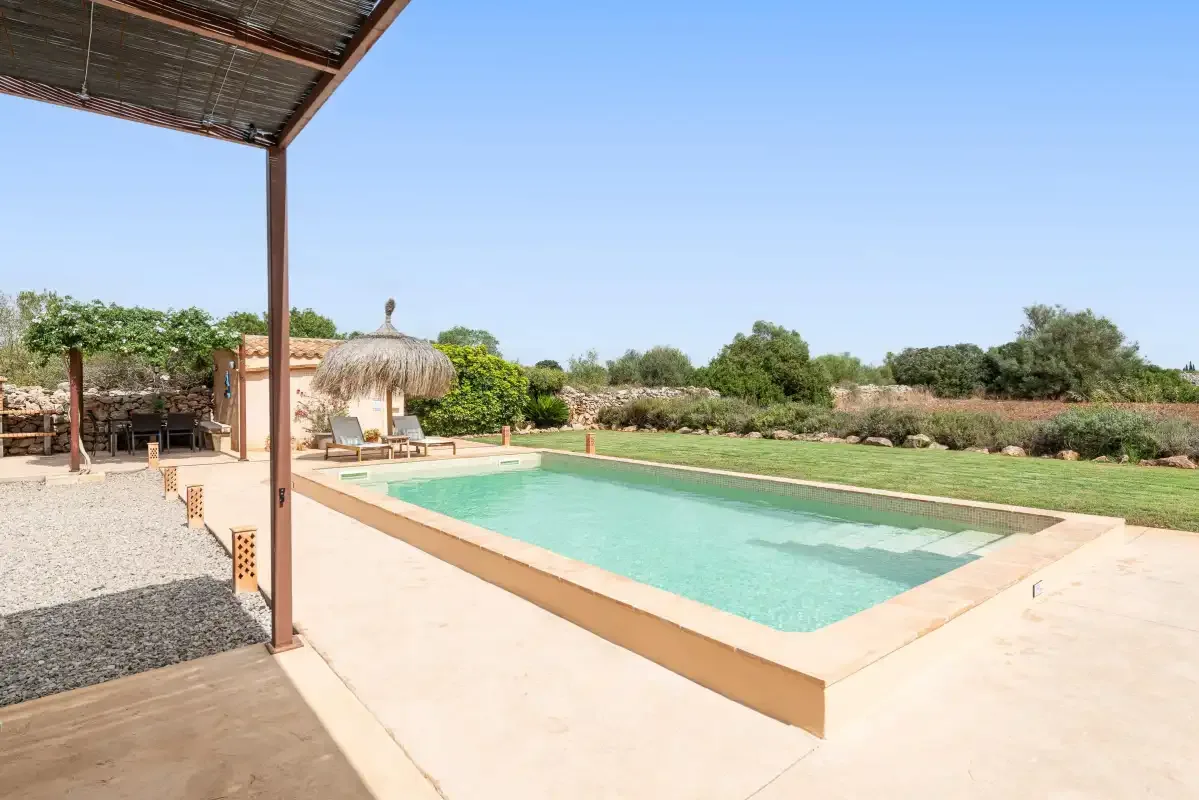 An outdoor swimming pool sits beside a shaded patio and landscaped garden.