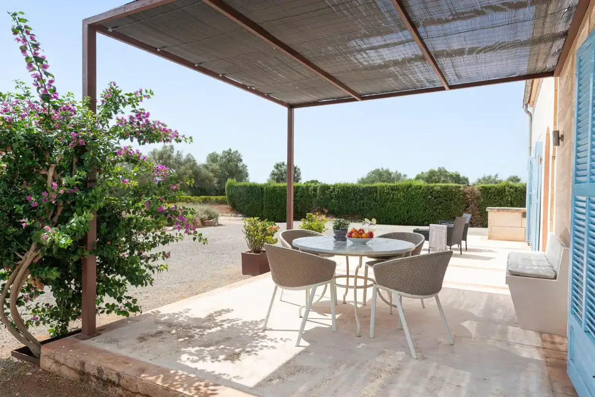 A shaded outdoor dining area with patio seating beside flowering shrubs.