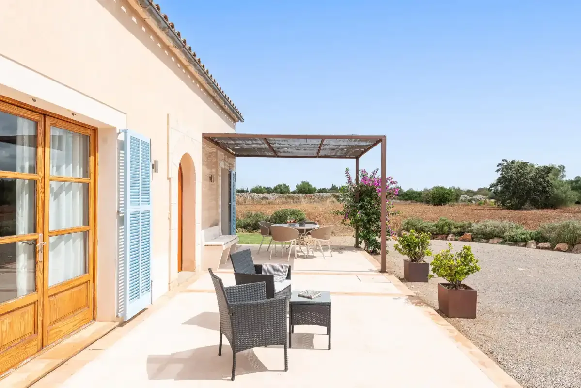 A sunny patio beside a house, with outdoor seating under a pergola.