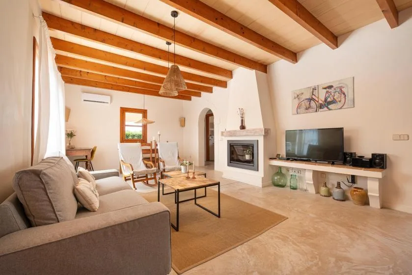 A bright living room with exposed ceiling beams, seating, and a television.