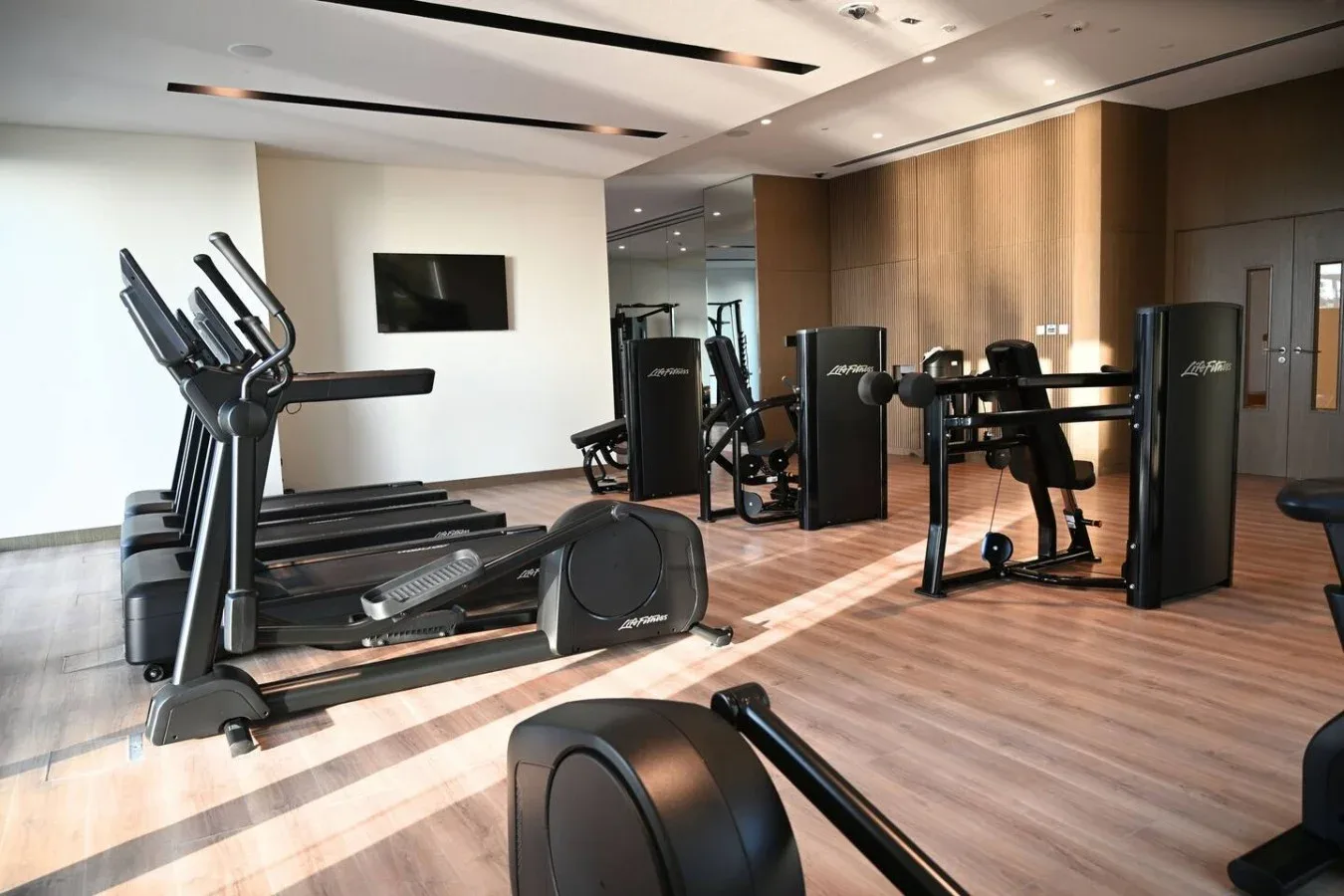 Un gimnasio con cintas de correr, equipos de ejercicio y una pared revestida de madera.