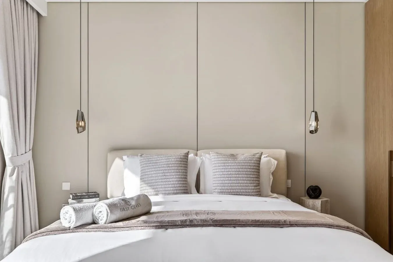 Un dormitorio con una cama bien tendida y dos lámparas colgantes.