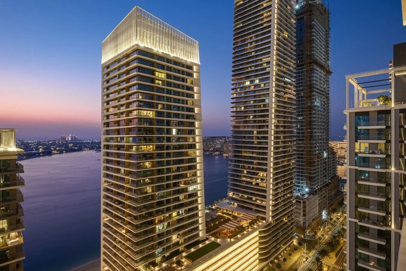 Horizonte urbano al anochecer, con edificios altos iluminados junto a un río.
