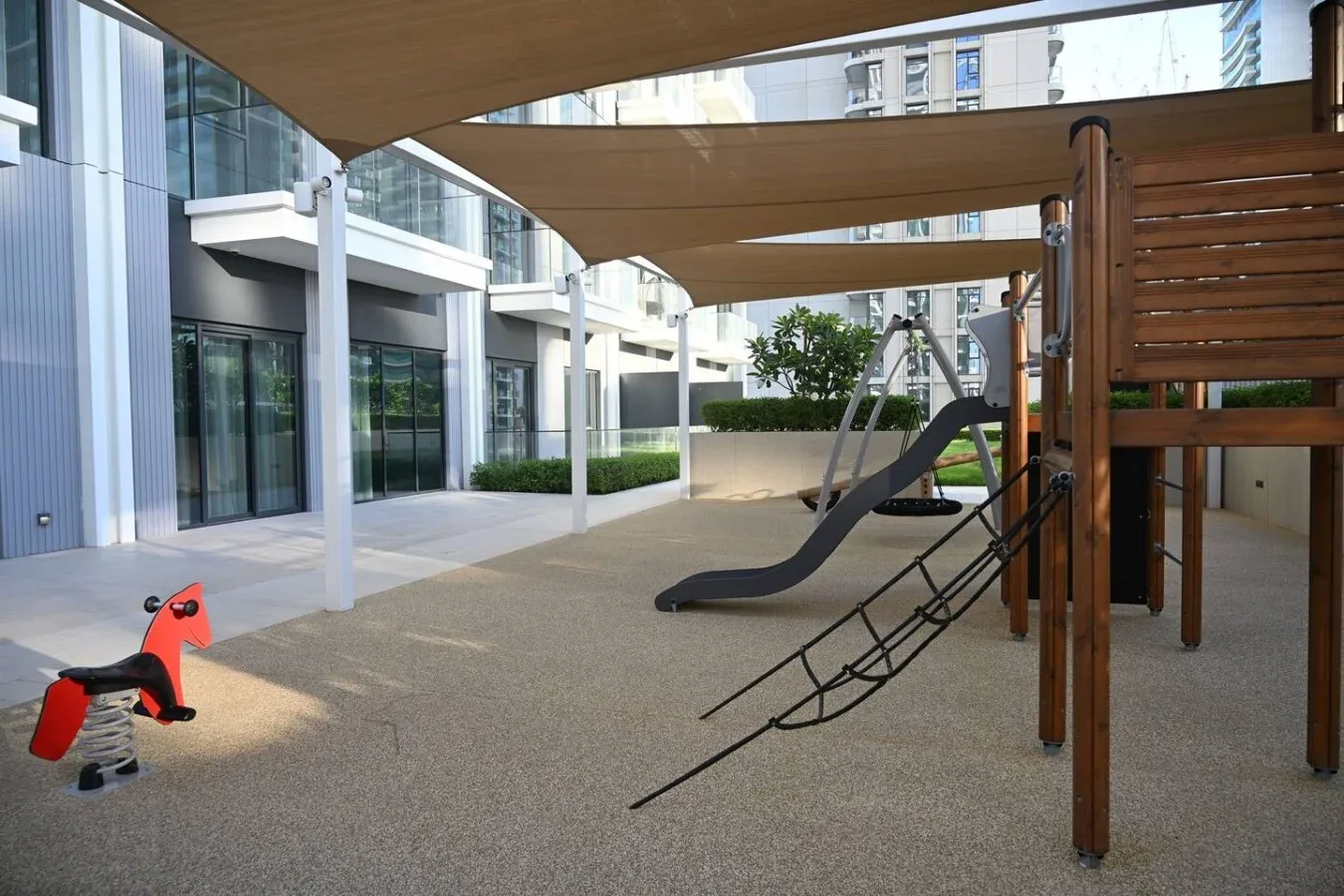 Un área de juegos cubierta con un tobogán y equipo para trepar junto a un edificio moderno.