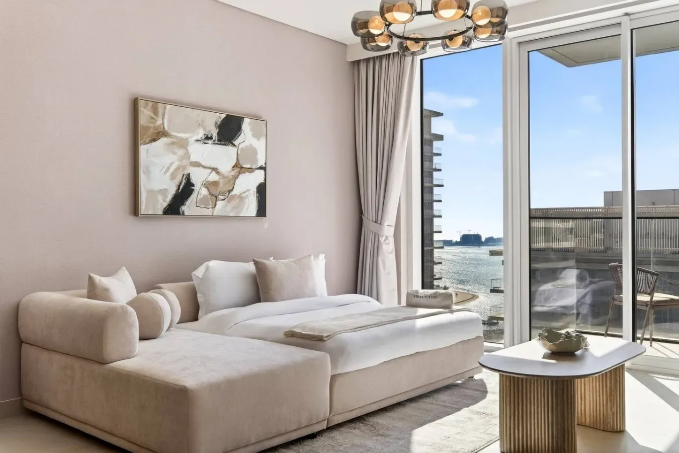 Una sala luminosa tiene un sofá seccional color crema y grandes ventanas con vistas al agua.