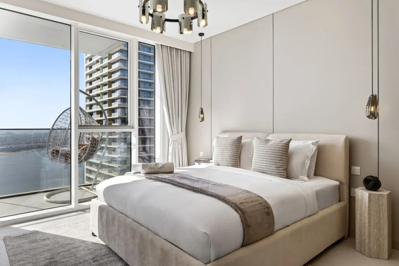 Un dormitorio luminoso con una cama tendida junto a ventanas de piso a techo.