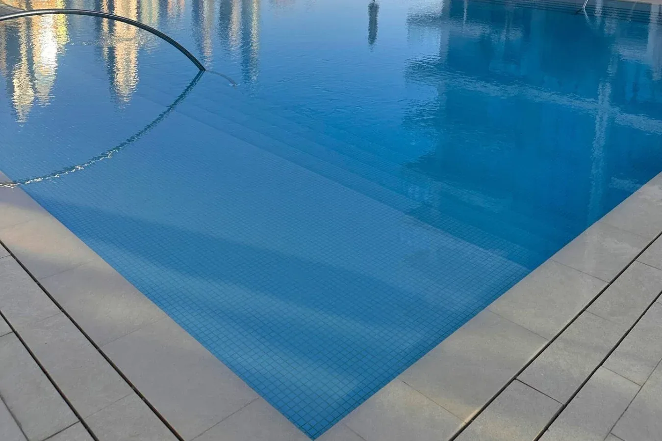 Una piscina de agua azul con un borde pavimentado de color claro.