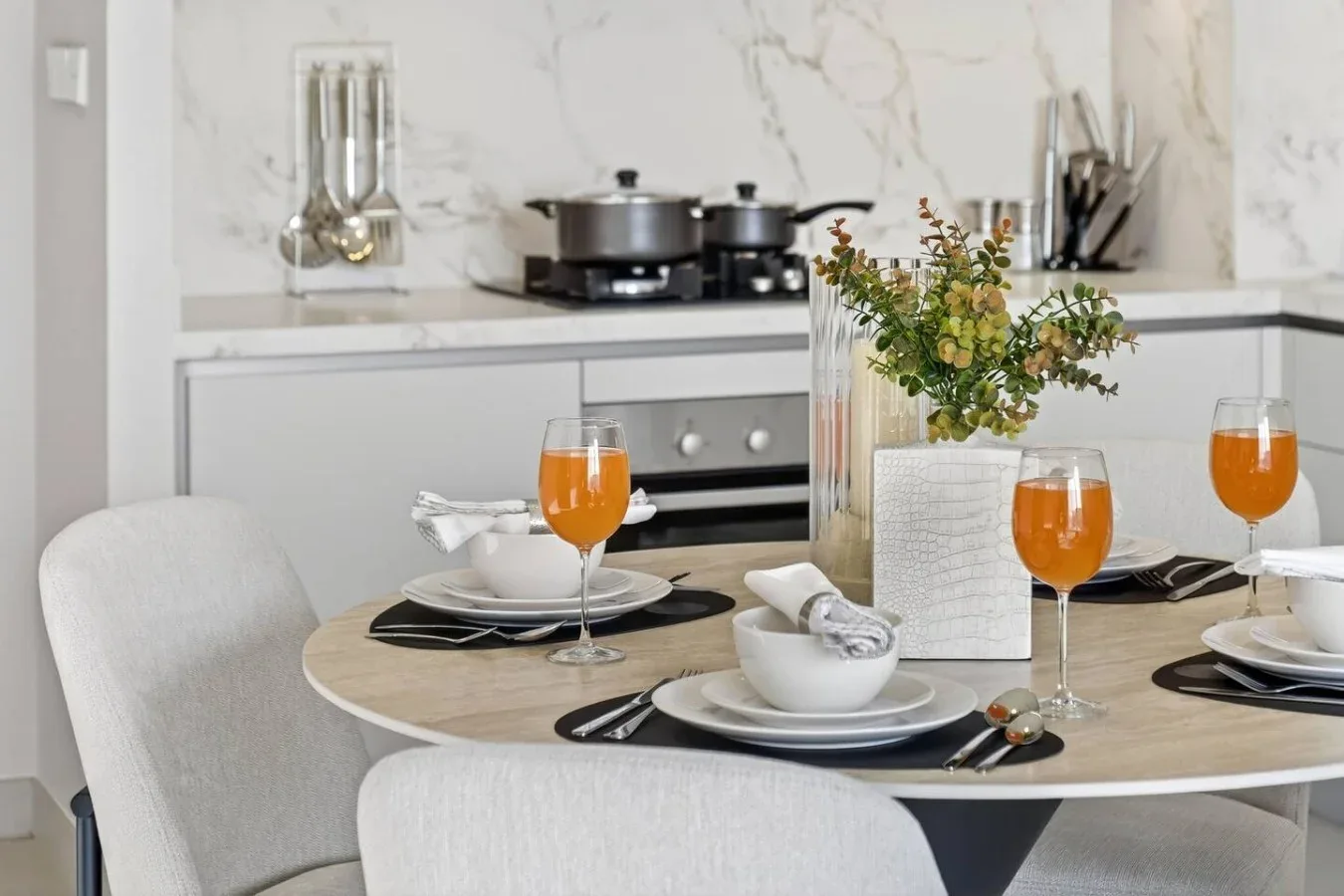 Una mesa puesta con platos y vasos está junto a una cocina luminosa.