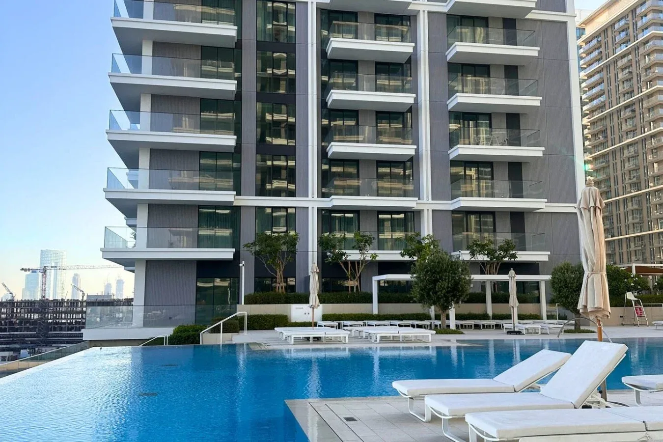 Una piscina al aire libre con tumbonas está frente a un edificio de apartamentos moderno.