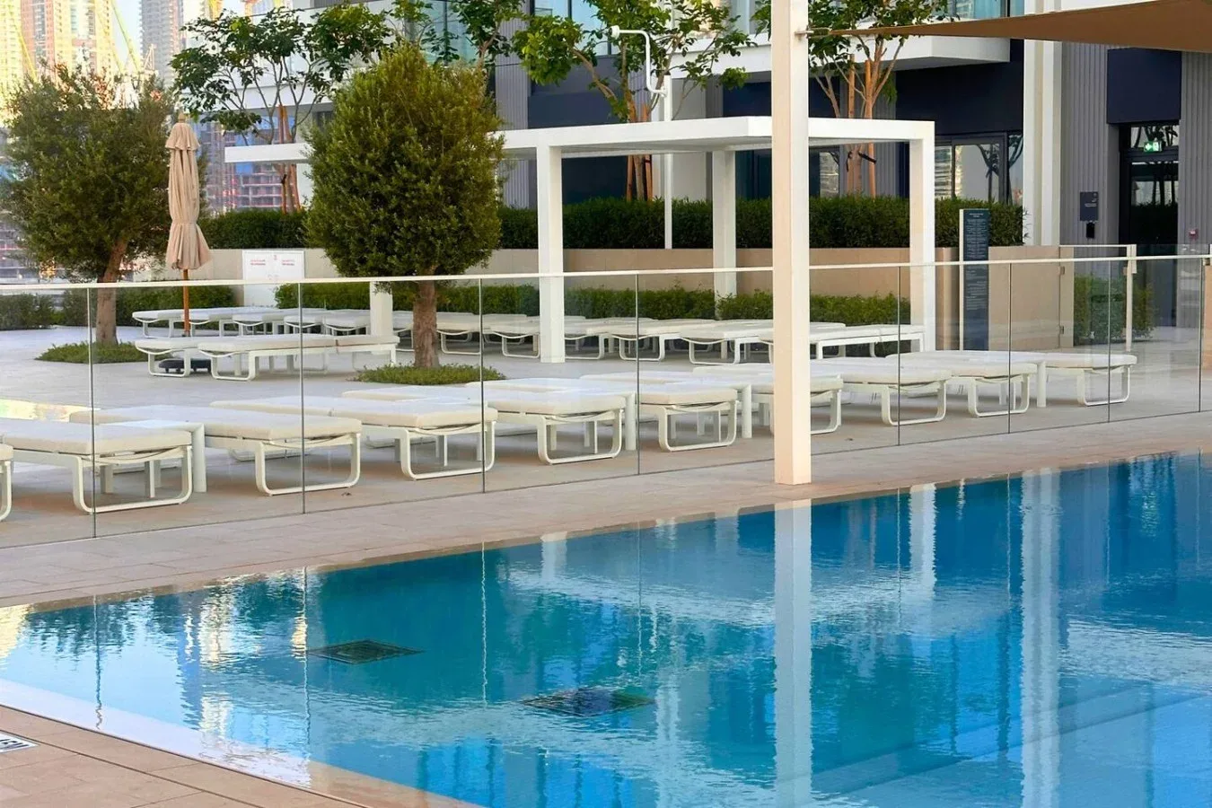 Una piscina al aire libre junto a una terraza con tumbonas y árboles.