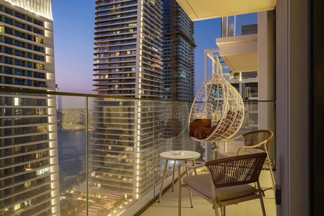 Una zona de estar en un balcón con una silla colgante y vistas a edificios altos cercanos.