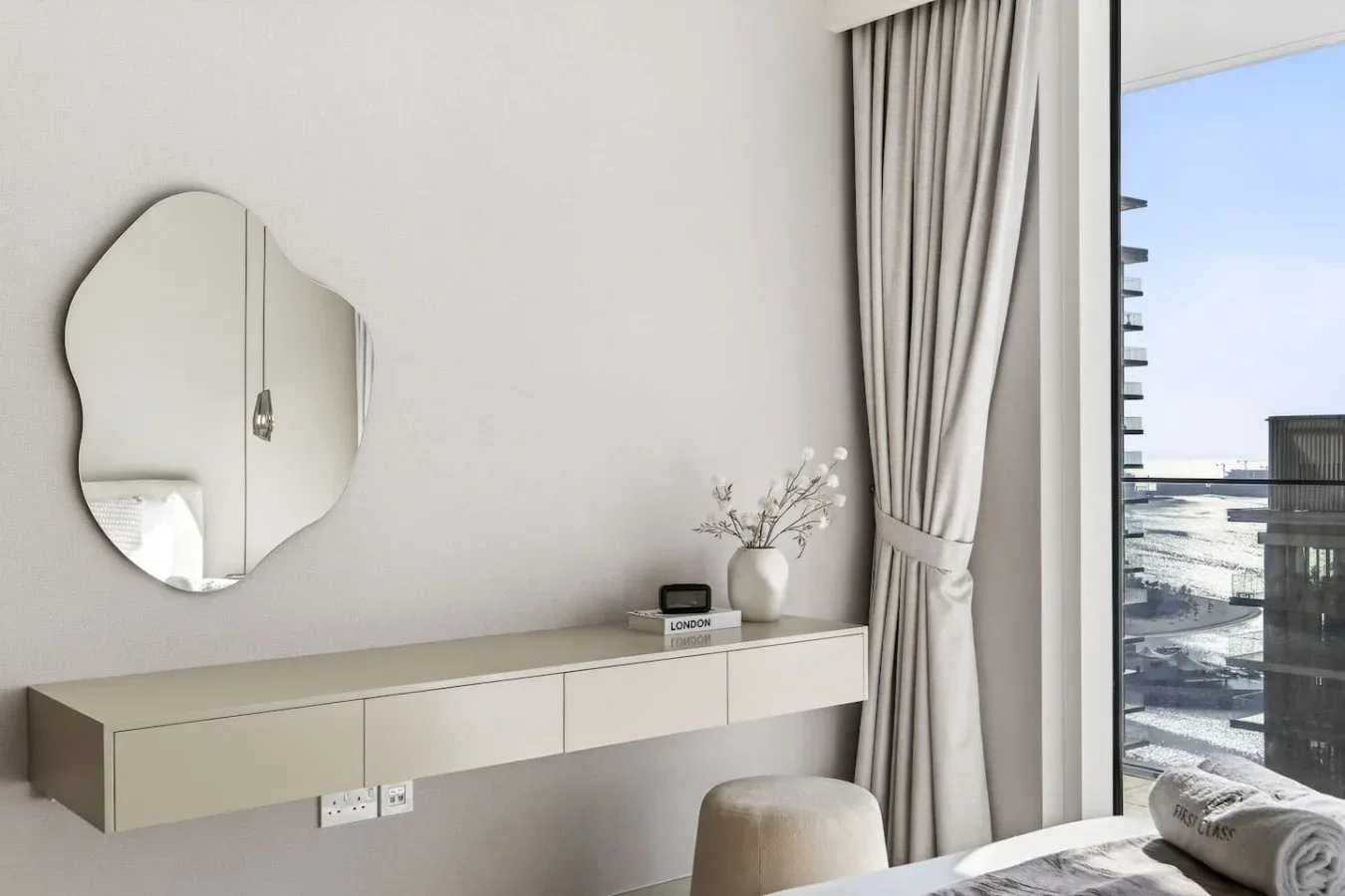 Zona de tocador en un dormitorio con espejo, mueble flotante y ventana.