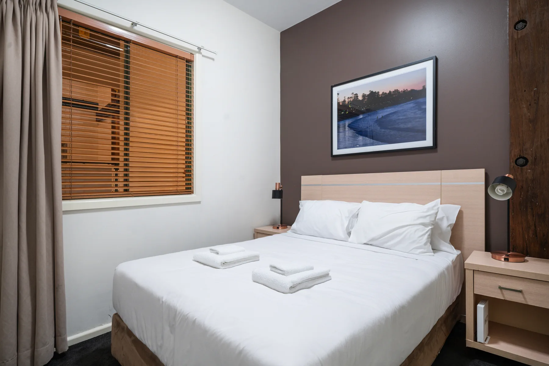 A bedroom with a neatly made bed and wooden blinds on the window.