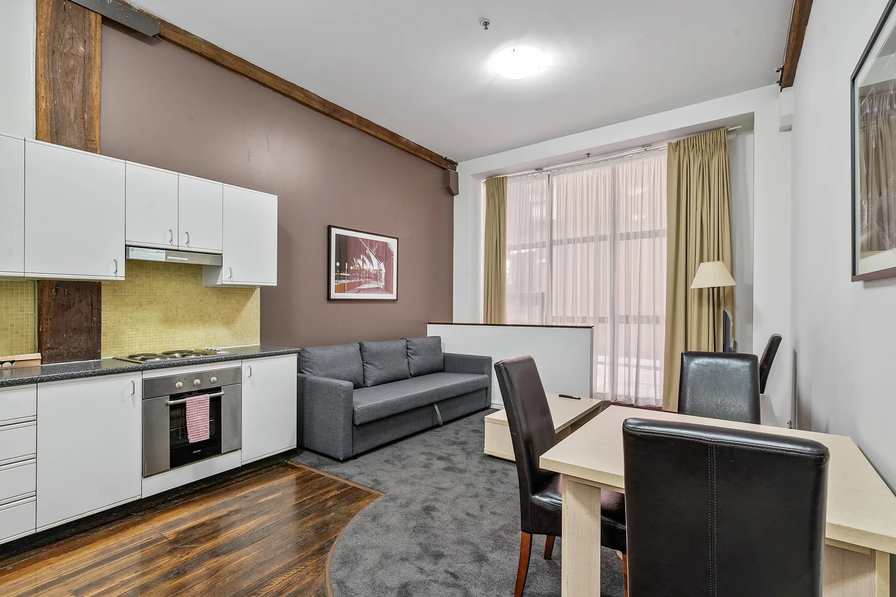 A room with a kitchen area, seating, and a dining table beside a curtained window.