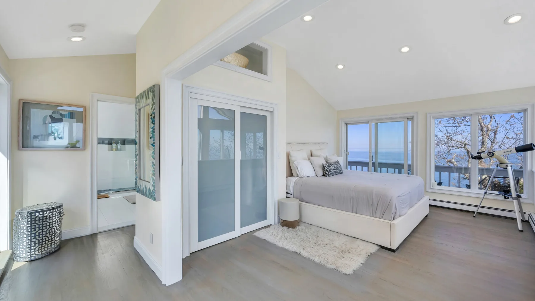 Un dormitorio luminoso con una cama junto a grandes ventanas con vistas al agua.