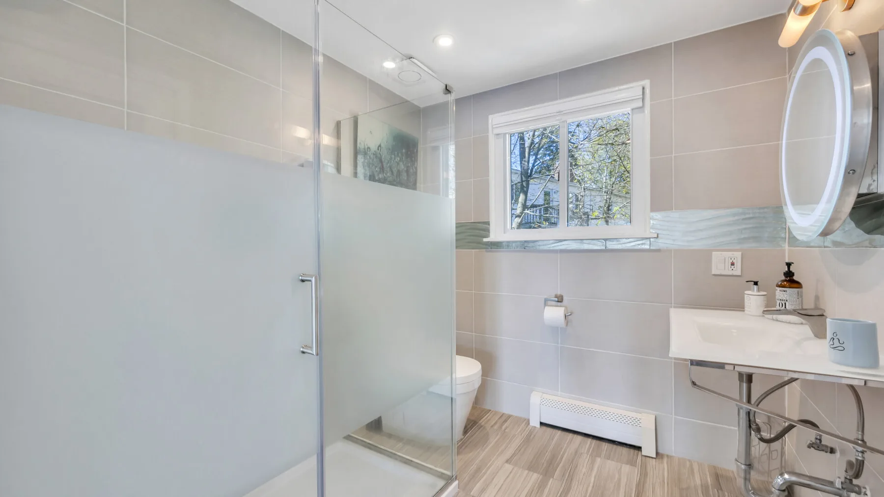 Un baño alicatado con ducha de vidrio, lavabo y ventana.