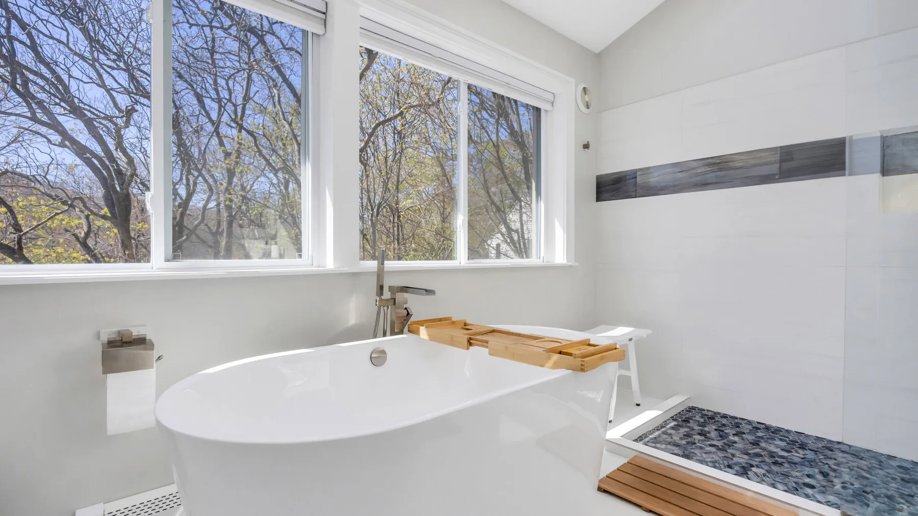 Un baño luminoso con una bañera grande junto a amplias ventanas.