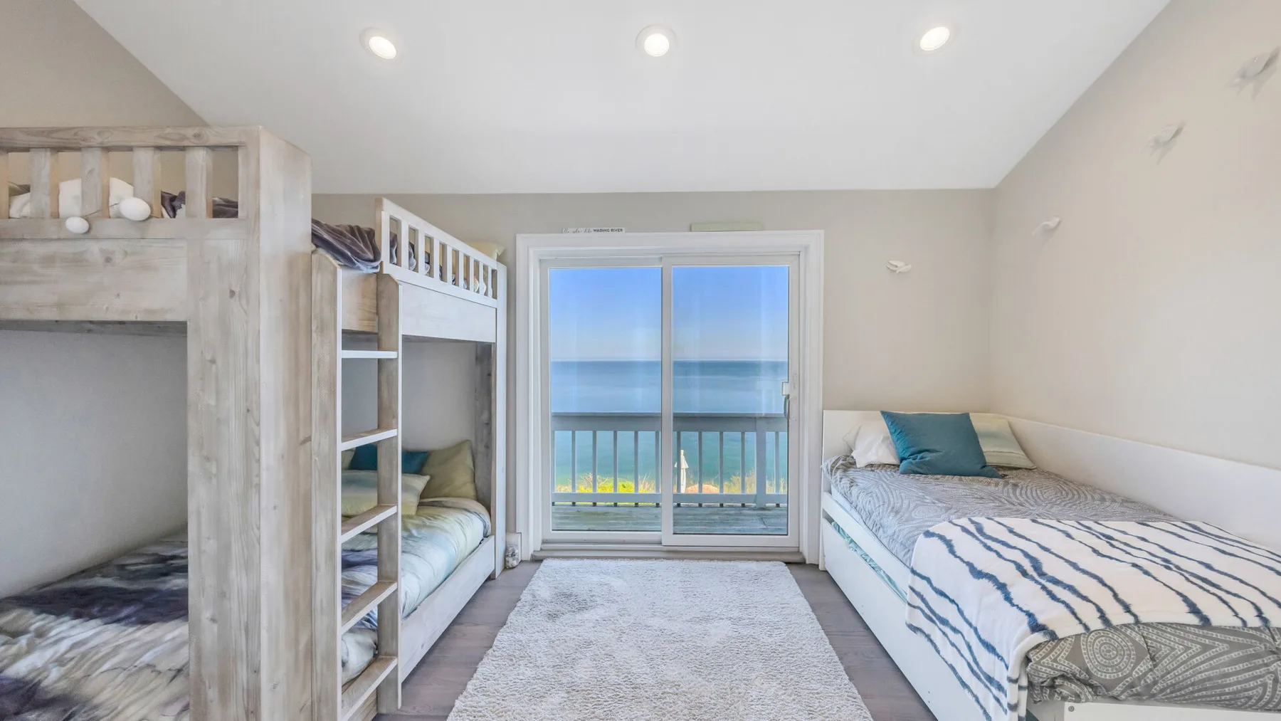 Un dormitorio con literas, una cama más grande y una puerta al balcón con vistas al agua.