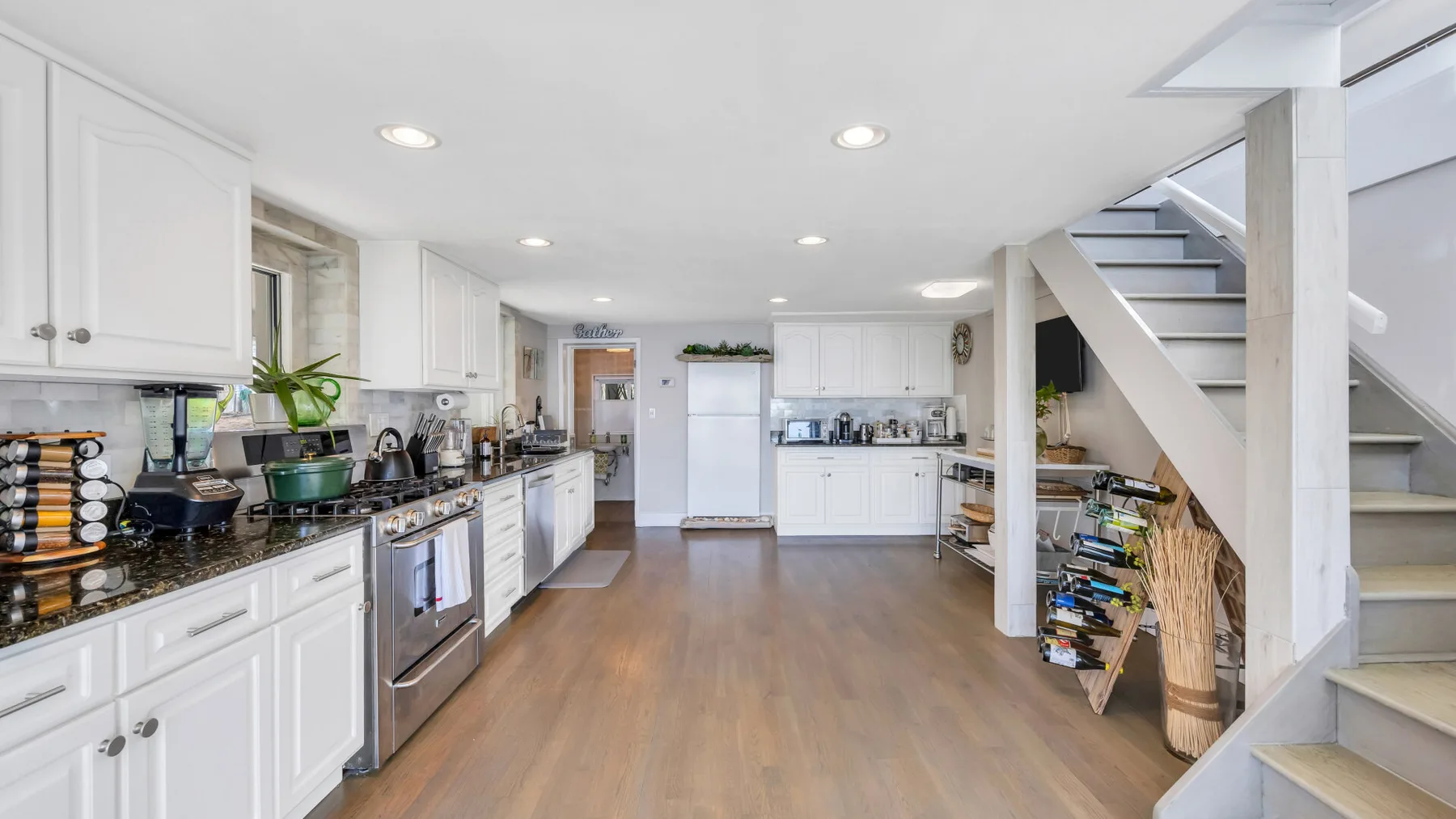 Una cocina luminosa con gabinetes blancos, electrodomésticos de acero inoxidable y un largo pasillo con piso de madera.