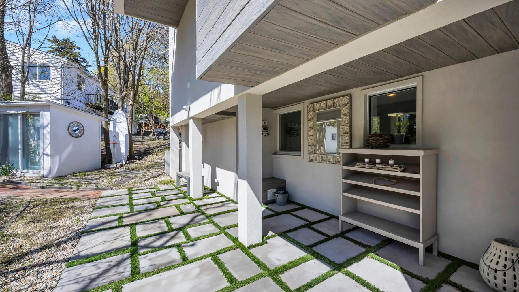 Un patio exterior cubierto tiene una barra integrada y losas cuadradas con césped entre ellas.