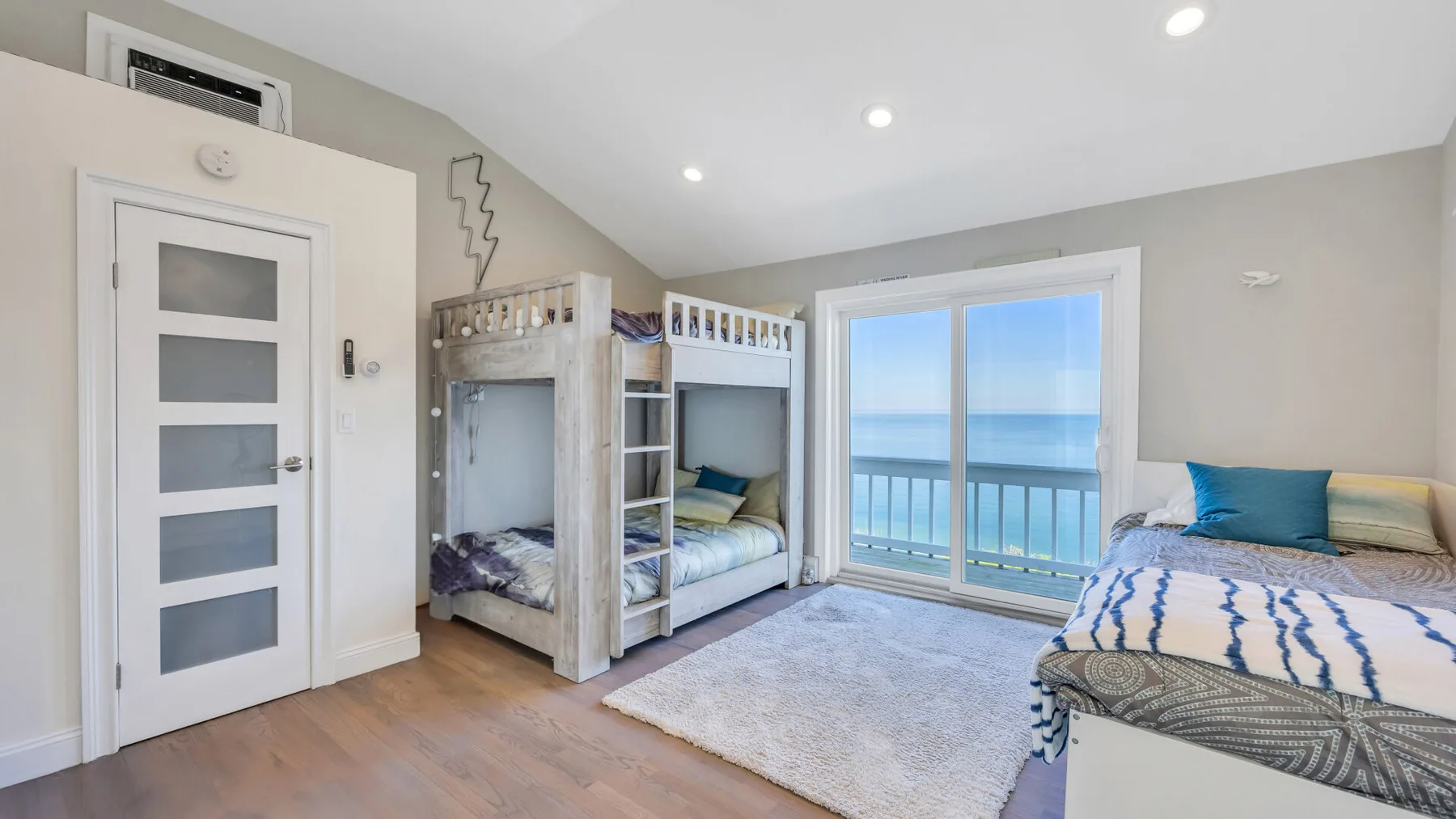 Un dormitorio luminoso con literas, otra cama y una ventana amplia con vistas al océano.