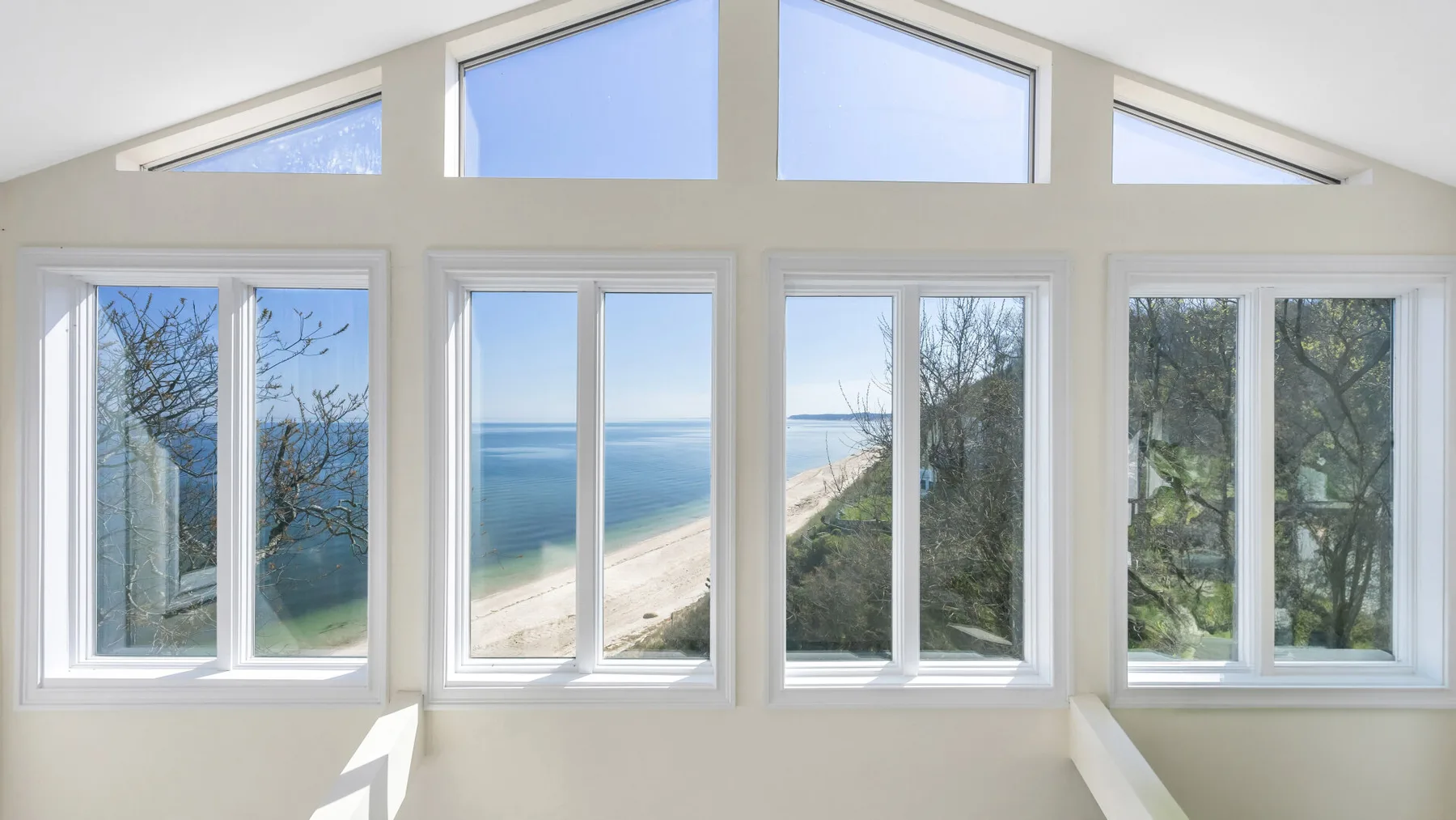 Una habitación luminosa con grandes ventanas que dan al océano y la costa.