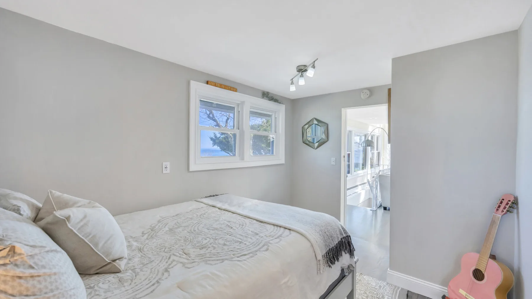 Un dormitorio con una cama, dos ventanas y una guitarra apoyada contra la pared.
