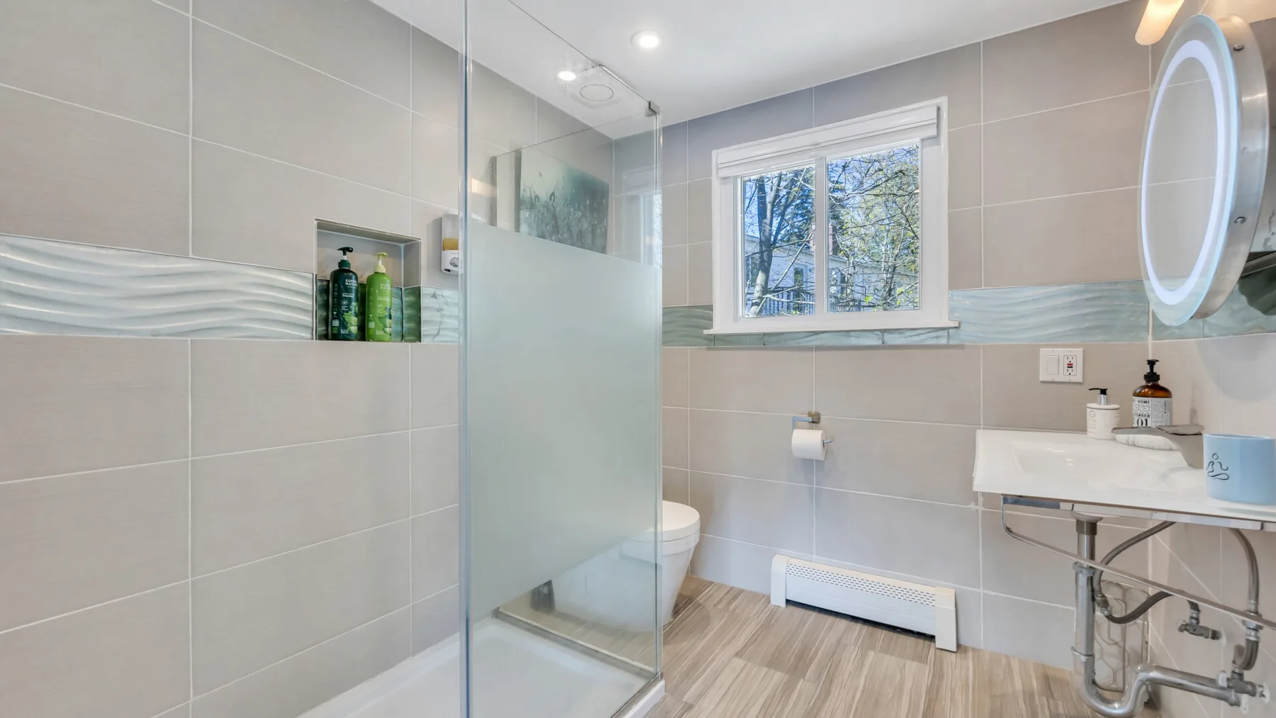 Un baño luminoso con azulejos, una ducha de vidrio y una ventana.