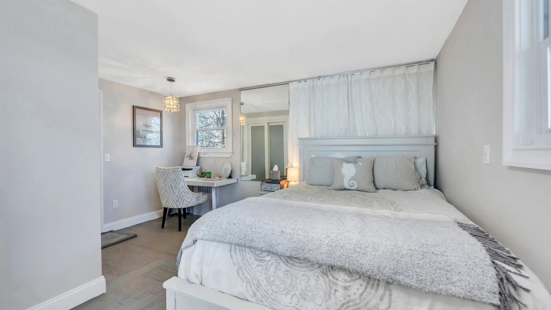 Un dormitorio luminoso con una cama bien tendida y un escritorio pequeño junto a la ventana.