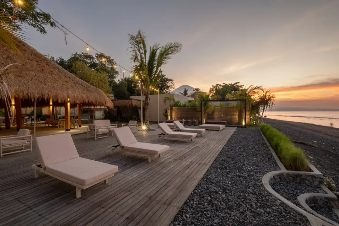 Una terraza junto al mar con asientos reclinables mira hacia el agua al atardecer.