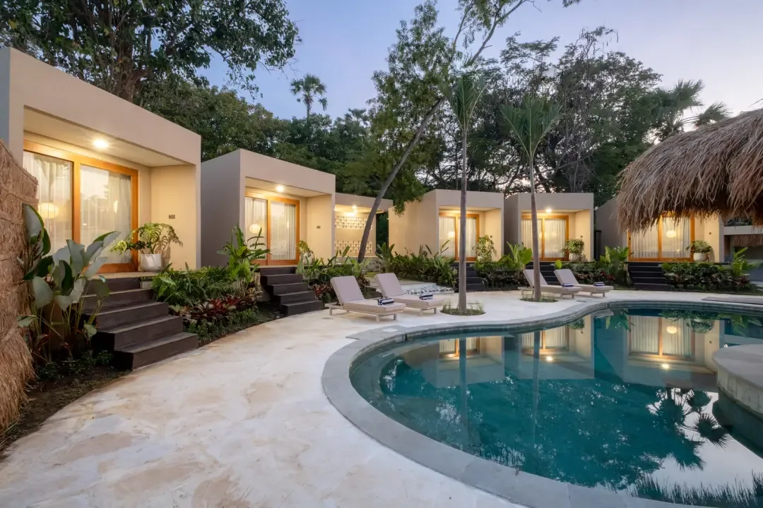 Una piscina en el patio está junto a habitaciones tipo bungalow y asientos al aire libre.