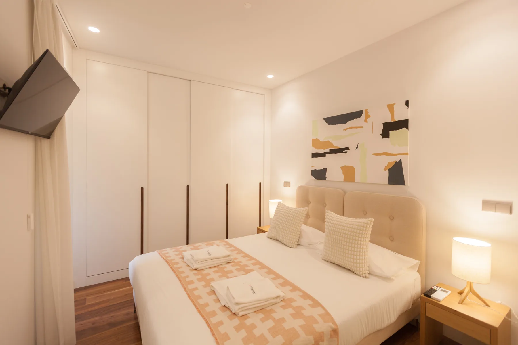 Un dormitorio con la cama bien arreglada y una obra abstracta sobre el cabecero.