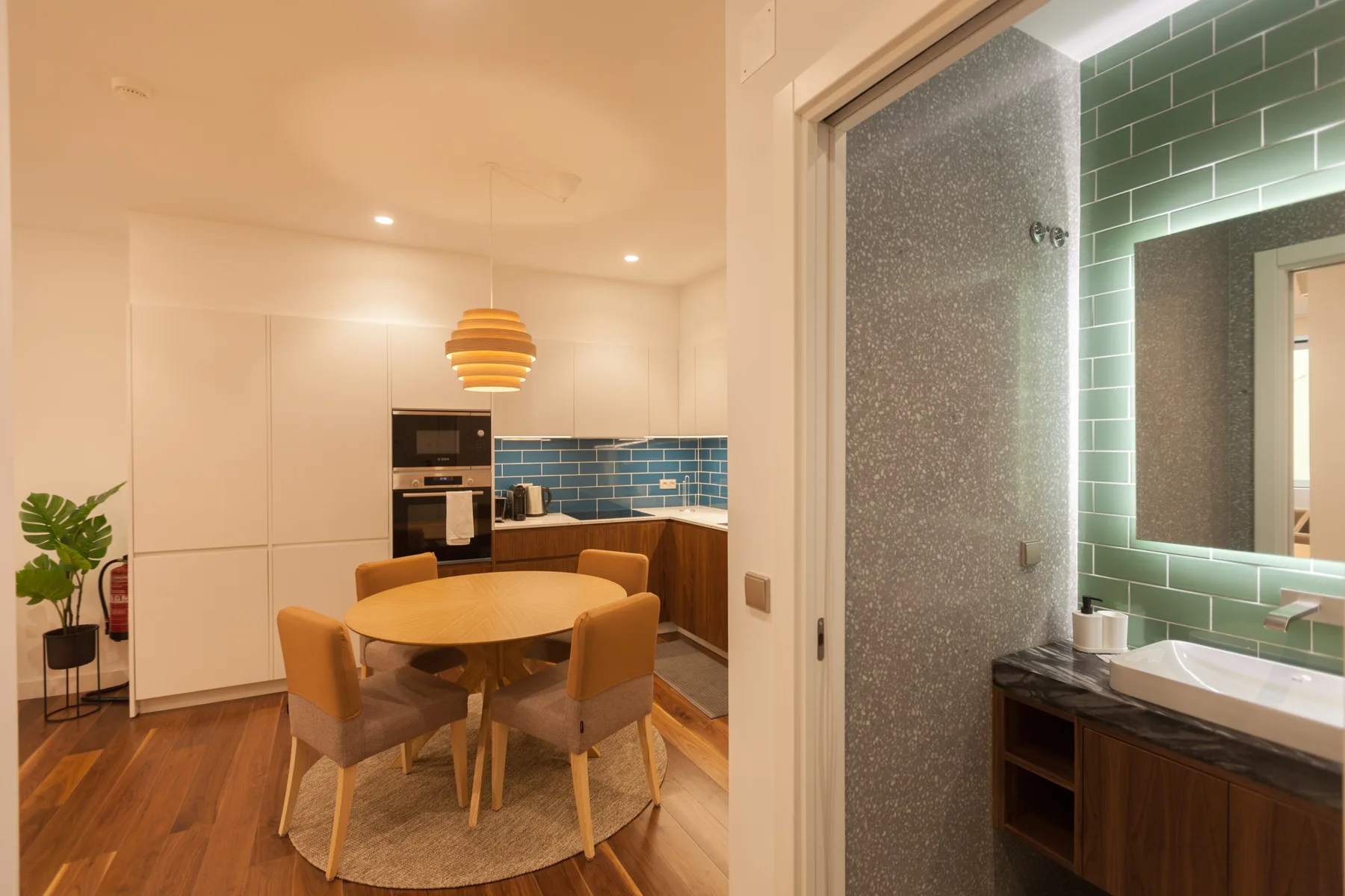 Un comedor y una cocina compacta junto a un baño con paredes de azulejos verdes.