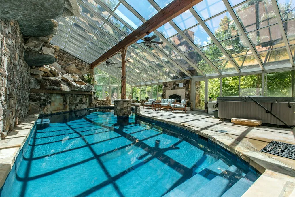 Una piscina cubierta bajo un techo de cristal, con paredes de piedra y asientos.