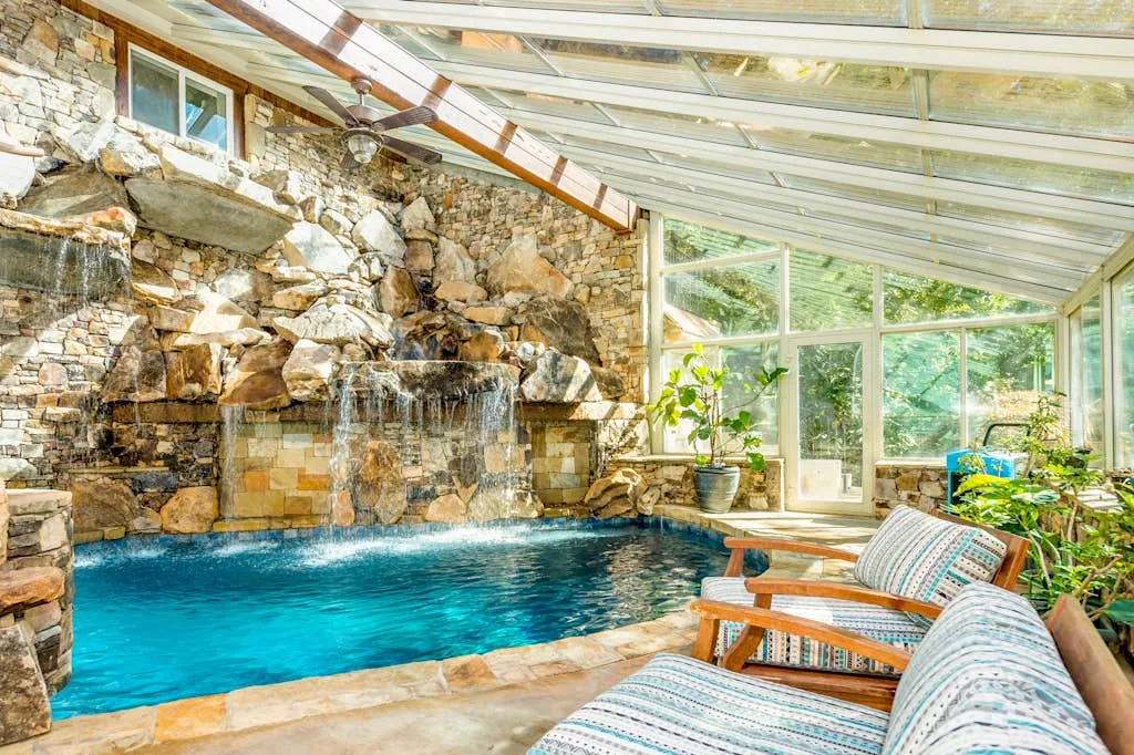 Una piscina interior está junto a una cascada de piedra, con asientos cercanos.