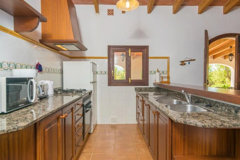 Una cocina con armarios de madera, encimeras de piedra y una ventana sobre el fregadero.
