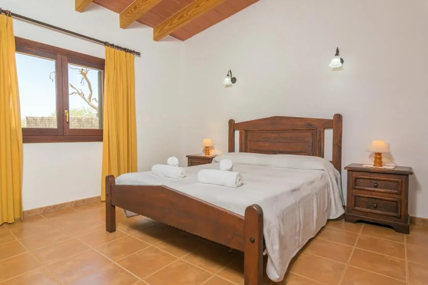 Un dormitorio con una cama de madera, mesitas de noche y una ventana con cortinas amarillas.