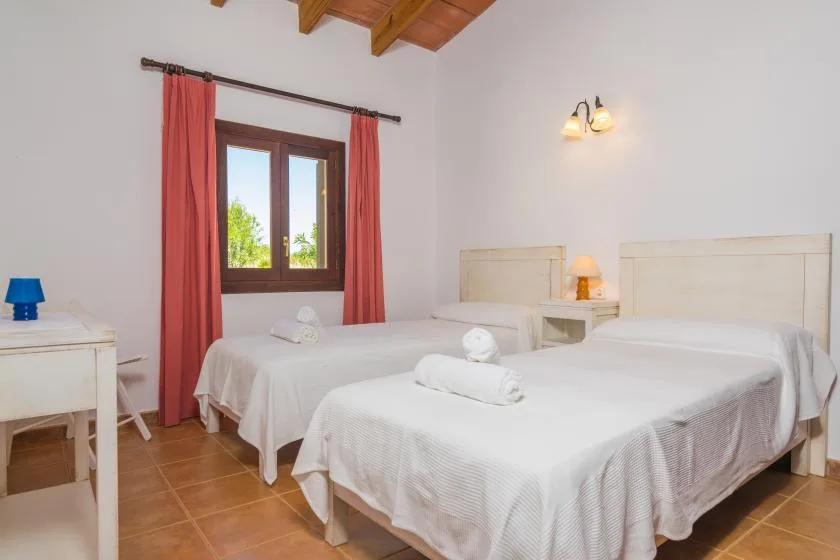 Un dormitorio con dos camas, una ventana y cortinas rojas.