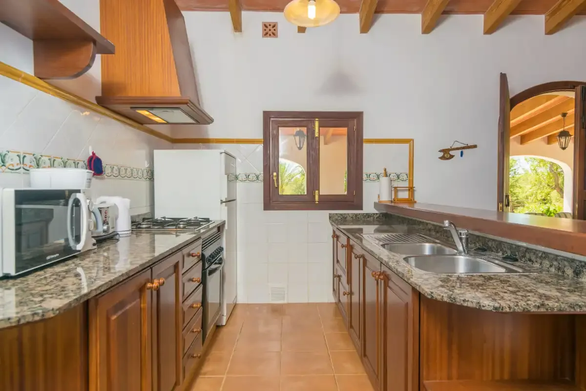 Una cocina con armarios de madera, encimeras de piedra y una ventana central.