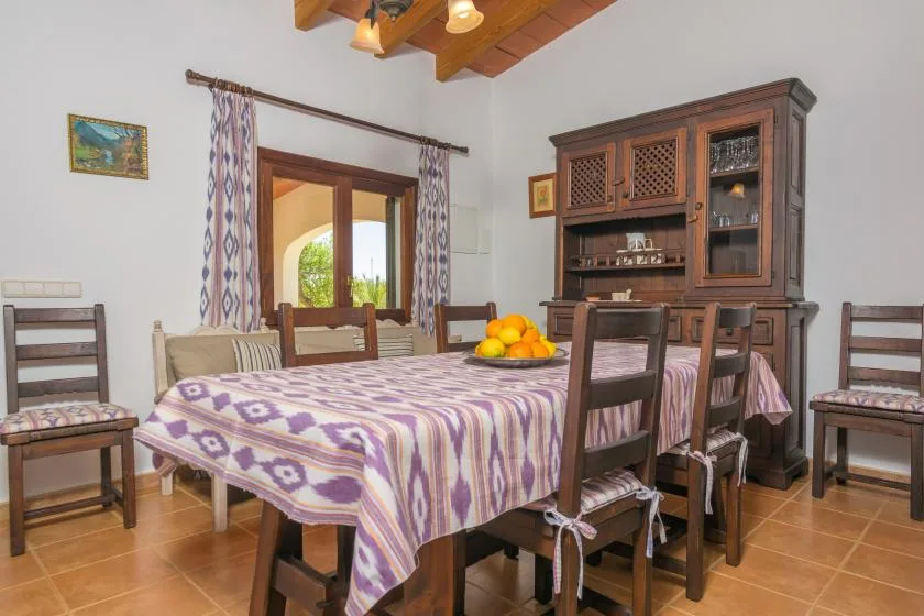 Comedor con una mesa grande cubierta con un mantel estampado y sillas de madera.
