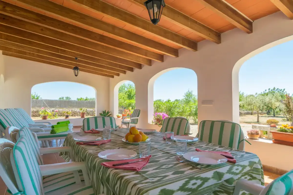 Una terraza cubierta con una mesa larga y vistas al jardín.